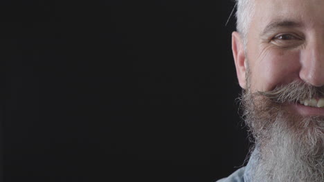 half face portrait of mature bearded man looking at camera smiling cheerful enjoying success satisfaction caucasian male on black background copy space close up