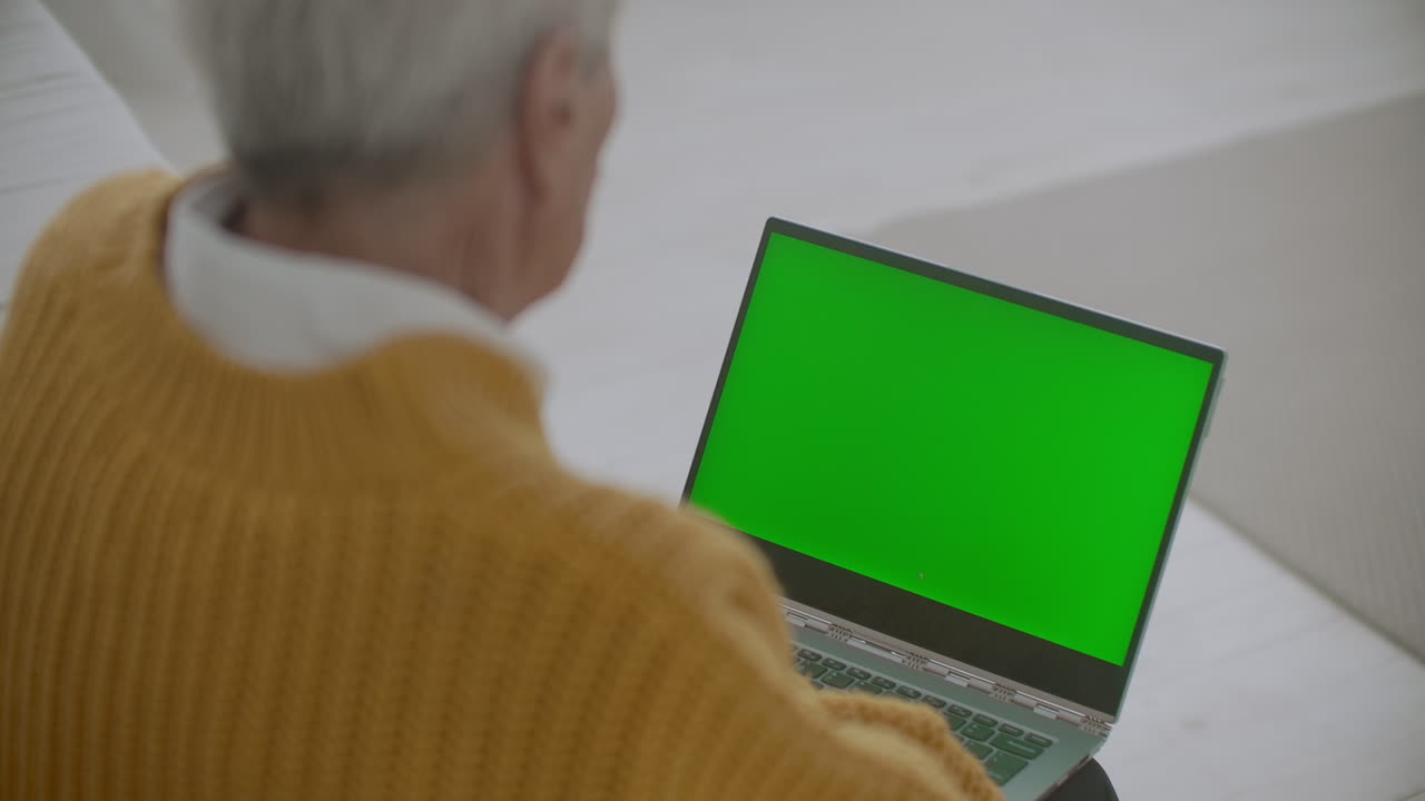 una mujer mayor mira un monitor con una pantalla verde y habla a través de un enlace de video con su nieta o hija o un médico. ayuda de video para los ancianos. la abuela usa una computadora portátil