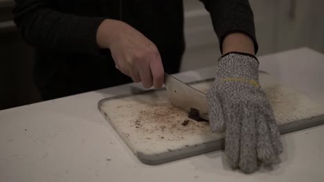 a young girl cuts up dark chocolate before melting it for millionaire shortbread cookies while wearing safety gloves-5