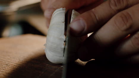 close up slicing whole garlic bulb in half with sharp knife on wood board