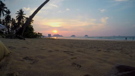 4k time lapse on beach with people as sunsets on horizon behind islands