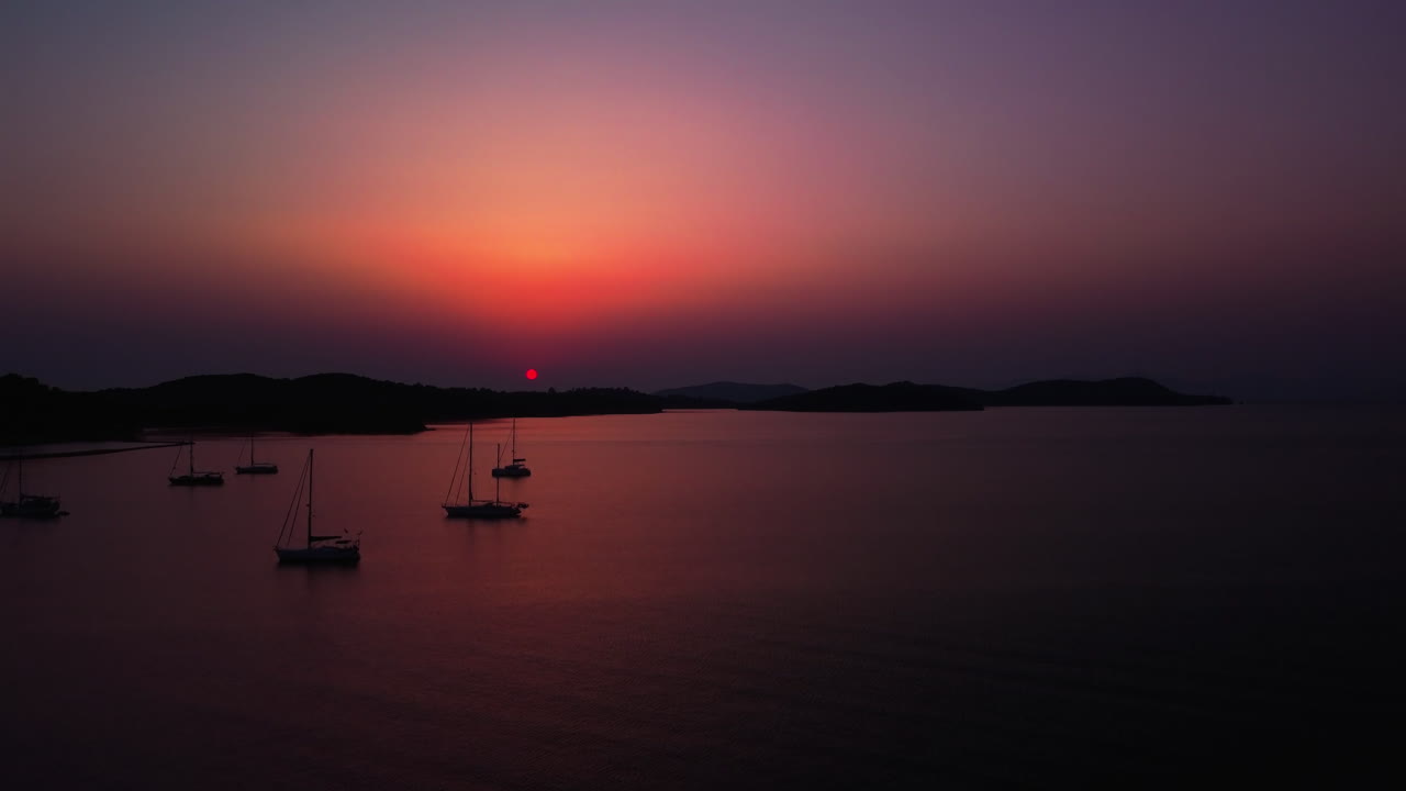 Sailboats in the Mediterranean sea with beautiful reflections of sunlight on the surface near Corfu Island - aerial, camera moving up.