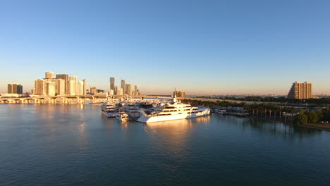 panoramic view of a city skyline during sunset time with golden light falling on buildings | cityscape background with yachts docked in bay video background