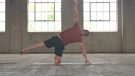 man in an industrial warehouse practicing yoga, the pose of forward wide legged fold.