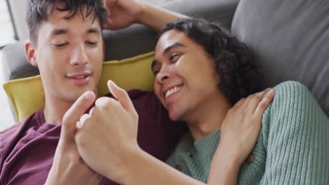 Happy-diverse-male-couple-lying-on-sofa,-embracing-in-living-room