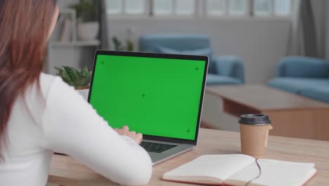 asian girl typing on computer keyboard of a laptop computer with green screen display at home, video in 4k