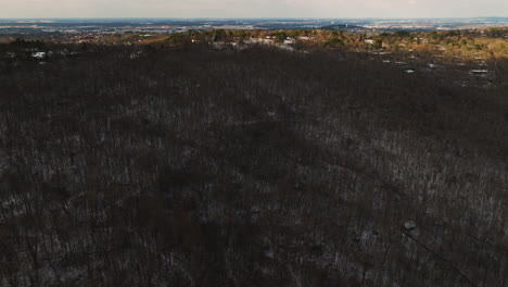 El-Denso-Bosque-Invernal-Del-Monte-Sequoyah-Con-Un-Paisaje-Urbano-Distante-Al-Atardecer,-Vista-Aérea