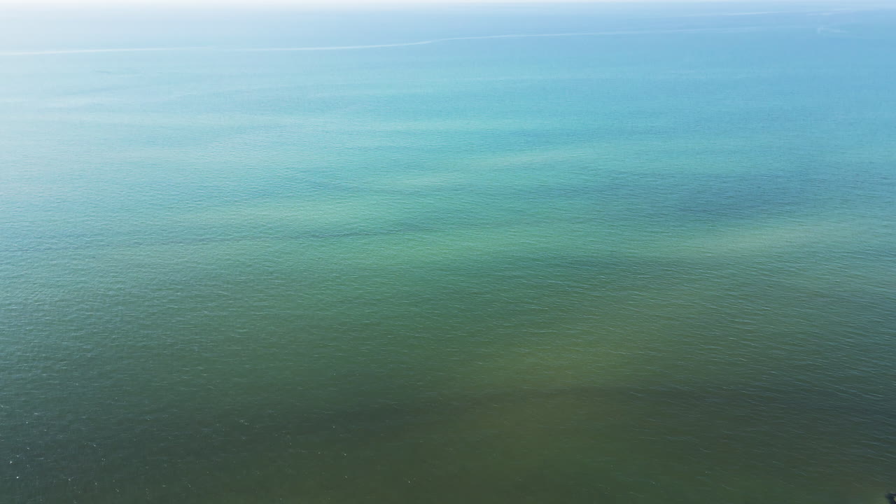 드론은 녹색 평온한 대서양 물을 가로질러 아래로 기울어져 표면에서 바다 벽과 해안 해변으로 파동됩니다.