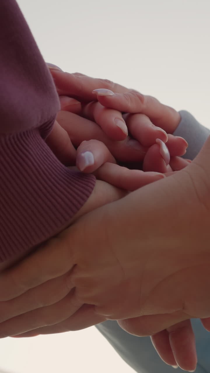 Primo piano di persone con felpe con cappuccio che uniscono le mani come membri di un team, con la luce del sole che crea un effetto luminoso intorno alle loro mani, a simboleggiare unità e lavoro di squadra in un ambiente esterno