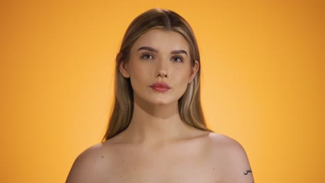 medium shot of a young naked and pretty woman sticking out her tongue while looking ironically into the camera in front of yellow background in slow motion