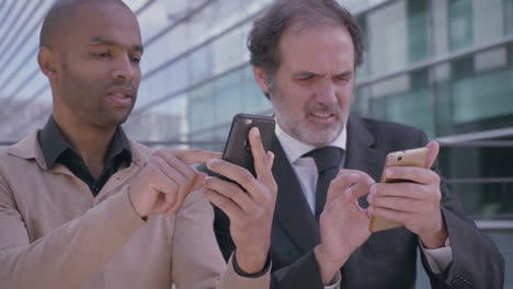 Confused-managers-using-smartphones-on-business-meeting-near-office-building