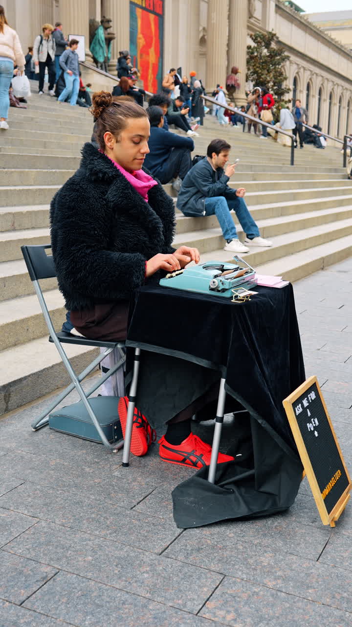 New York, USA, 2 Maret 2026: Penyair dengan mesin ketik antik di tangga Museum Seni Metropolitan. Seseorang duduk di meja dengan mesin ketik manual dan papan menawarkan puisi di depan bangunan megah