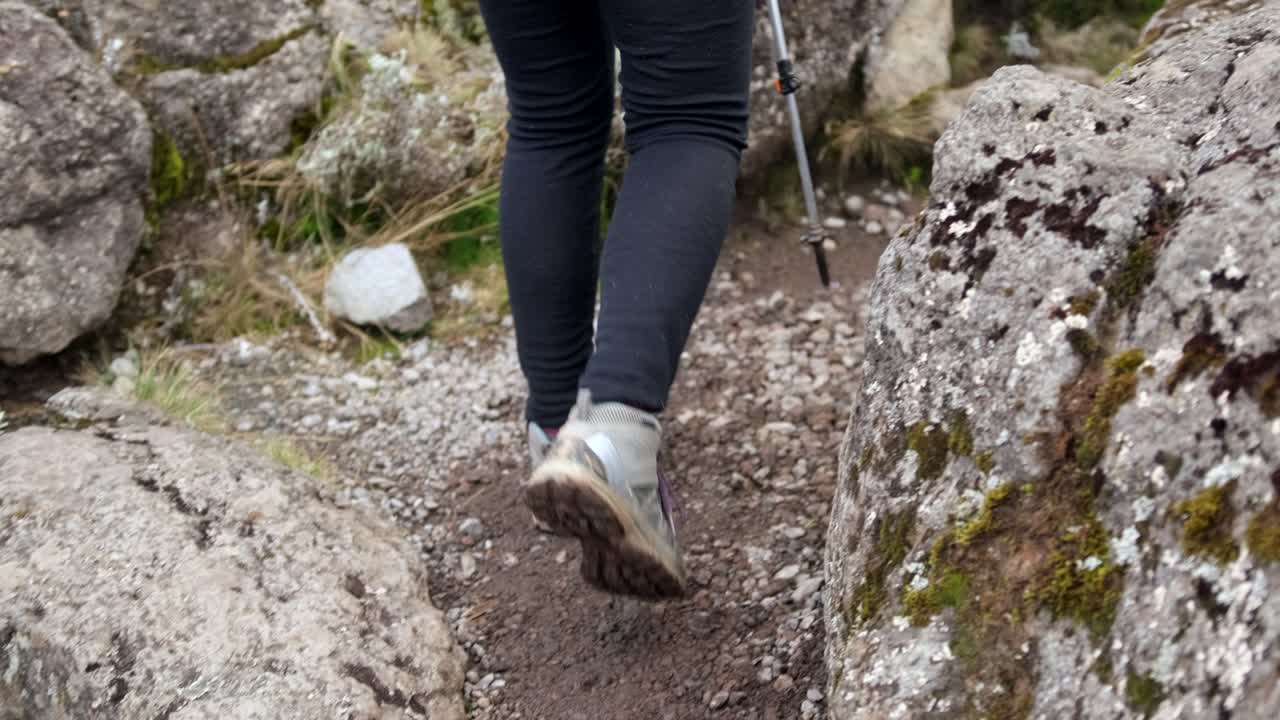 A tourist's foot in trekking boots climbs the rocks with trekking poles.