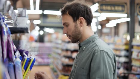 Nervous-man-doing-shopping.-Annoyed-man-trying-to-take-package-from-the-shelf.-Goods-falling-on-customer-in-supermarket