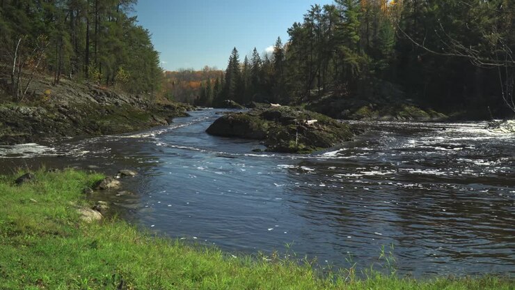 A river flowing around a rock island on a beautiful day with fall colors in the background