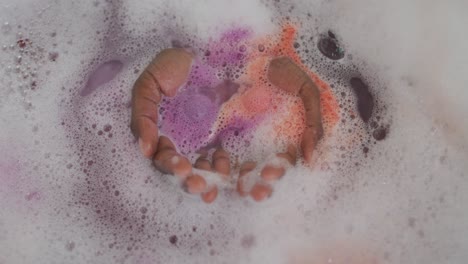 hands of african american attractive woman taking bath with foam, salt and rose petals