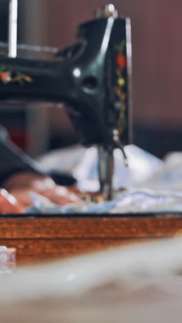 female tailor works on a sewing machine at her workplace. successful tailor sewing clothes in atelier with black sewing machine. vertical video