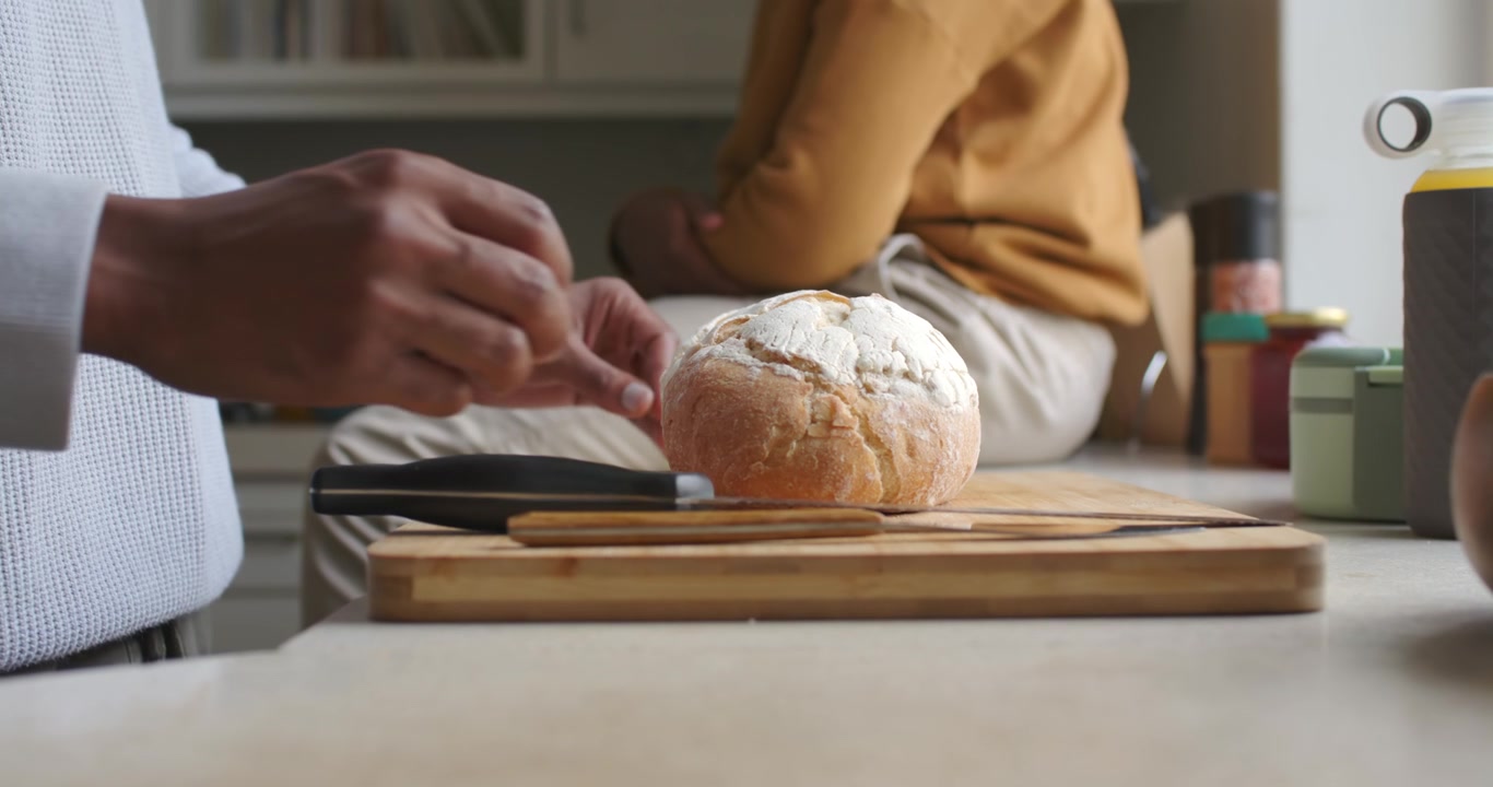 African American men entering holding loaf placing on board with knife preparing to cut at counter