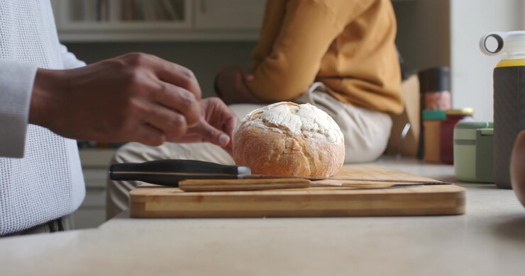 African American men entering holding loaf placing on board with knife preparing to cut at counter