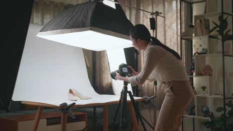 asian female photographer adjusting position of women's shoes while taking photos of them in home studio