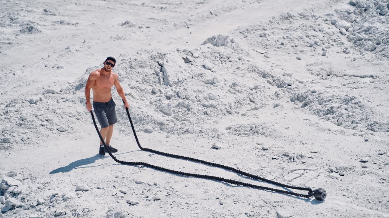 Happy sportsman finishing his workout with battle ropes outdoors. Topless athlete exercising with two ropes on the natural rocky background.