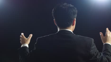 close up back view of asian speaker man in business suit showing index fingers up while speaking in the black screen studio