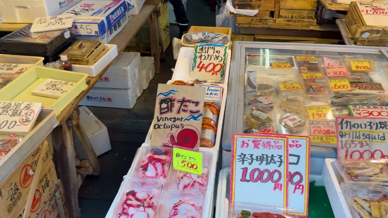屋外市場で、包装された様々なシーフードや魚がハイアングルパンショットで捉えられている。