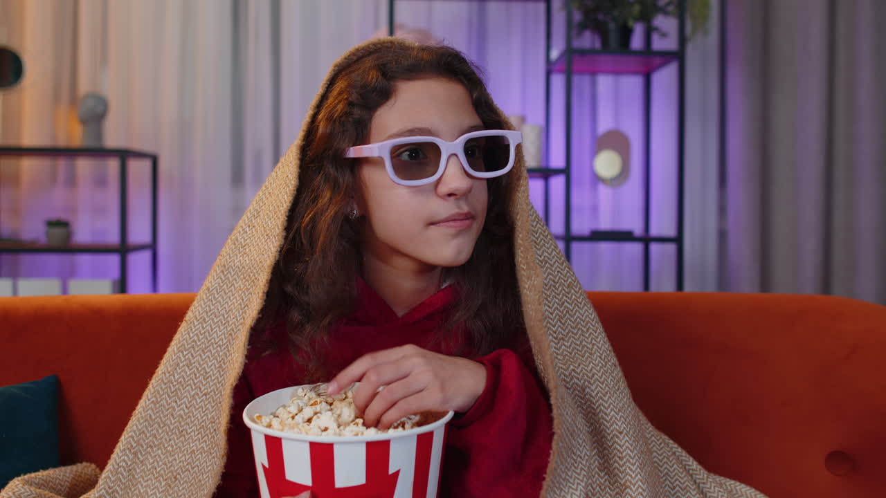 Oreteen girl eating popcorn watching interesting tv serial sport game online content on home couch