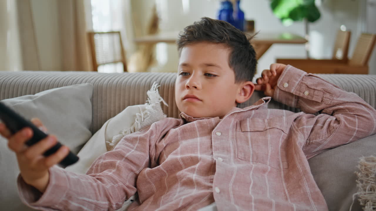 Lazy boy holding controller switching channels sofa closeup. Bored kid resting