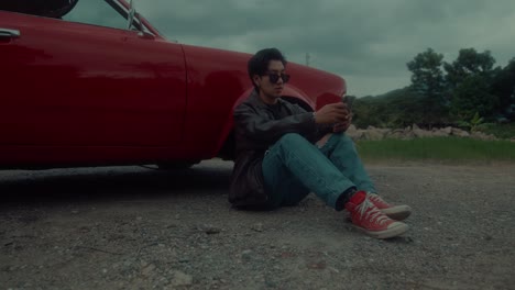man sitting by a red classic car with a phone