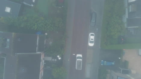 top down aerial of car driving through mist on a calm suburban road