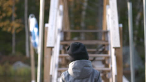 dolly shot, following a young boy walking on a hiking trail, bridge over river, beautiful autumn colors