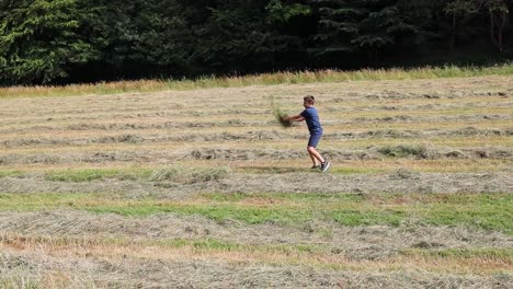 Niño-Tirando-Hierba,-Heno-Al-Aire-En-Un-Campo-Recién-Cortado