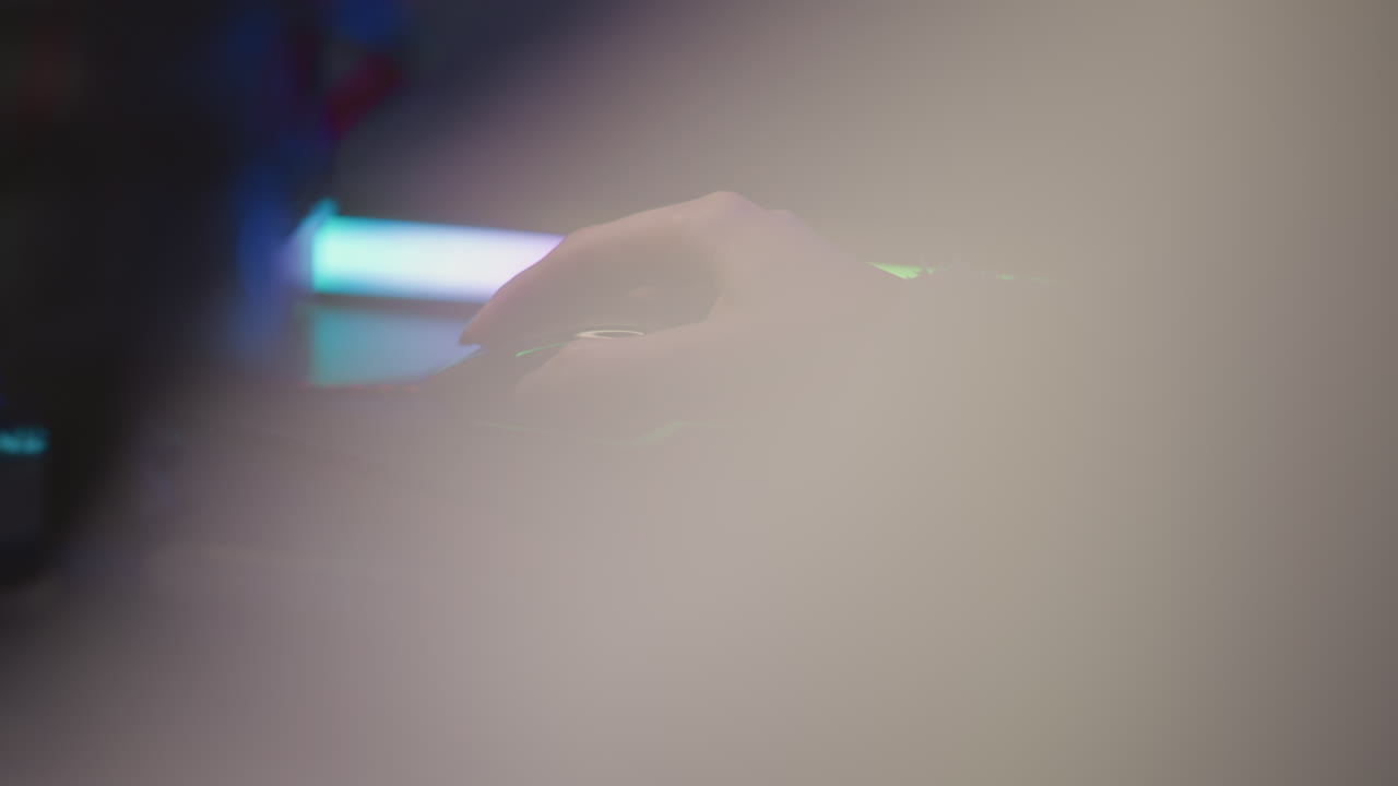 Close up woman hand with polished nail in fluffy sweater using mouse on black pad illuminated by soft pink and green hue light across fingers and desk suggesting