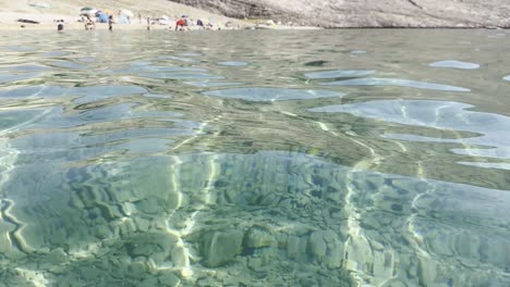 Clear-sea-water-with-barren-land-reflections-on-island-Pag's-beach-Metajna-in-Croatia,-summer