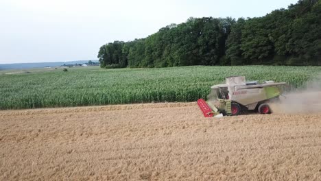 A-cinematic-4K-drone-shot-of-a-combine-harvester-harvesting-a-field-in-France,-showcasing-agriculture-with-an-epic-view-and-dramatic-dust