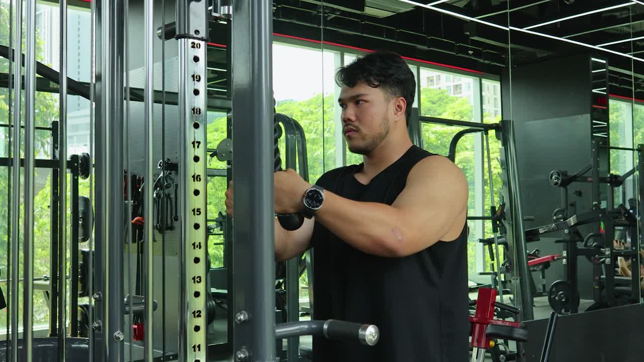 A muscular man in a sleeveless shirt executes a tricep rope pushdown on a cable pulley machine in a modern, well-lit fitness center with mirrored walls