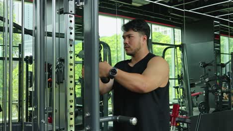 a muscular man in a sleeveless shirt executes a tricep rope pushdown on a cable pulley machine in a modern, well-lit fitness center with mirrored walls