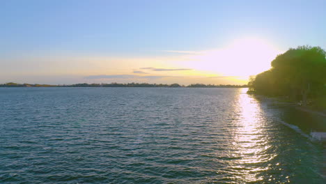 sunset over water revealed from behind trees. drone