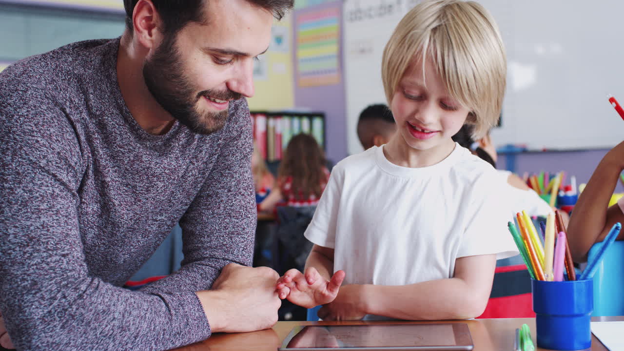 maestro de escuela primaria y alumno masculino dibujando usando una tableta digital en el aula