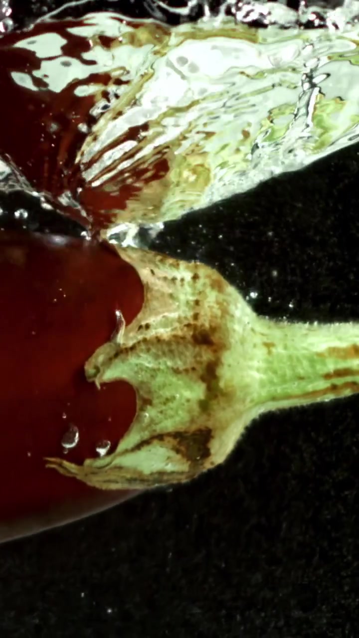 Rød peberfrugt plasker ned i vand i slowmotion