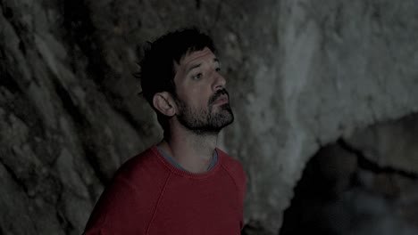 Caucasian-man-with-beard-looking-around-him-in-a-cave,-close-up