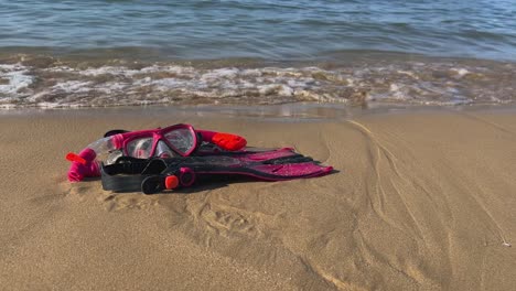 Flossen,-Maske-Und-Schnorchel-Liegen-Am-Sandstrand,-Während-Sich-Am-Ufer-Wellen-Brechen