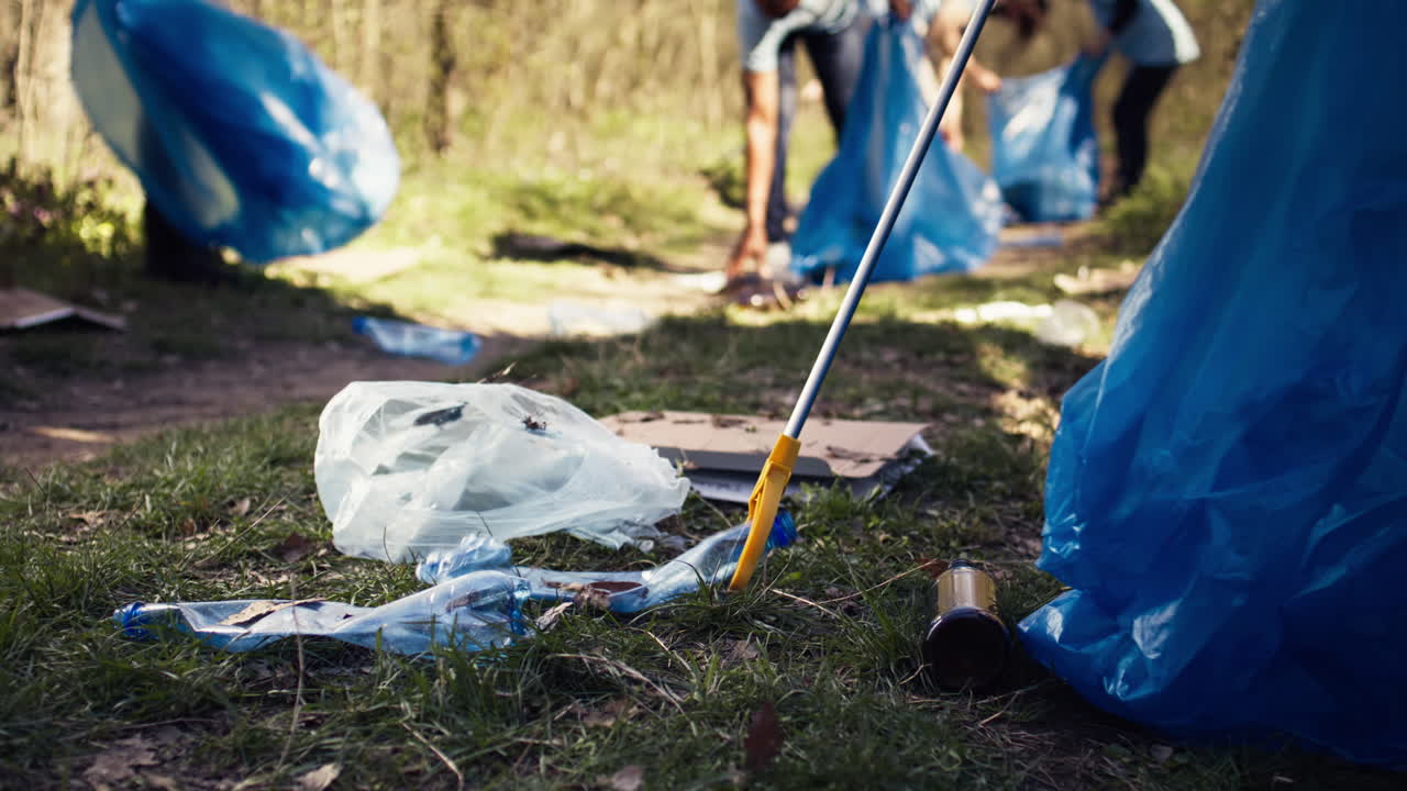 Volunteer using tongs tool to collect trash and plastic waste from the woods
