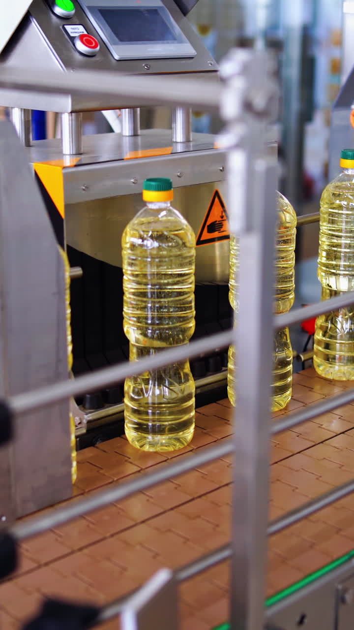 Modern factory of food oil production. Row of full plastic bottles of oil on a conveyor line. Fresh sunflower oil inside the automated manufacture. Vertical video