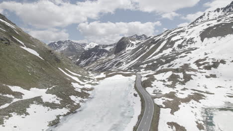 Drohnenschuss,-Der-An-Einem-Bewölkten-Und-Kalten-Tag-Mit-Klarem-Sichtprotokoll-über-Eine-Einzelne-Straße-Zwischen-Schneebedeckten-Bergen-Am-Fluela-Pass-In-Der-Schweiz-Fliegt