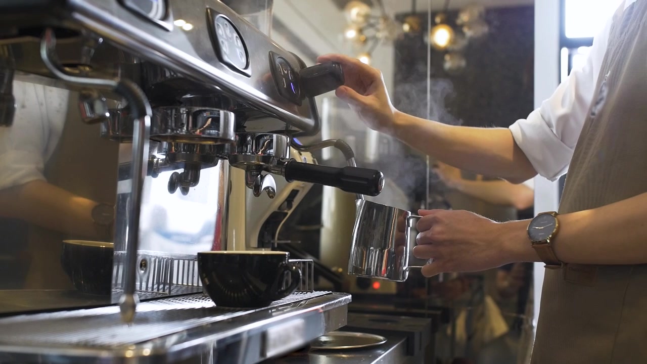 Barista di caffetteria monta il latte a vapore da aggiungere a cappuccino, latte o macchiato per un cliente. Slow motion, scorrimento a destra.