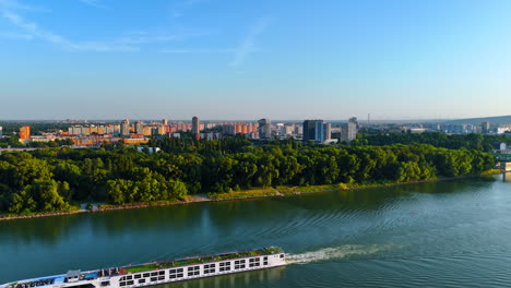 long tourist riverboat moves by the calm river. drone rises over the danube river revealing view on the cityscape of bratislava, slovakia