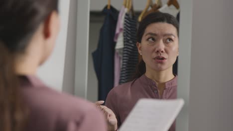 Young-Woman-In-Suit-At-Home-Practising-Job-Interview-Technique-Reflected-In-Mirror-