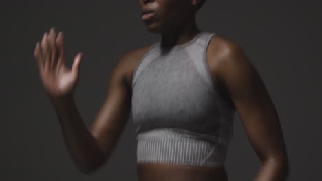 studio shot of woman wearing gym fitness clothing exercising running on the spot 2